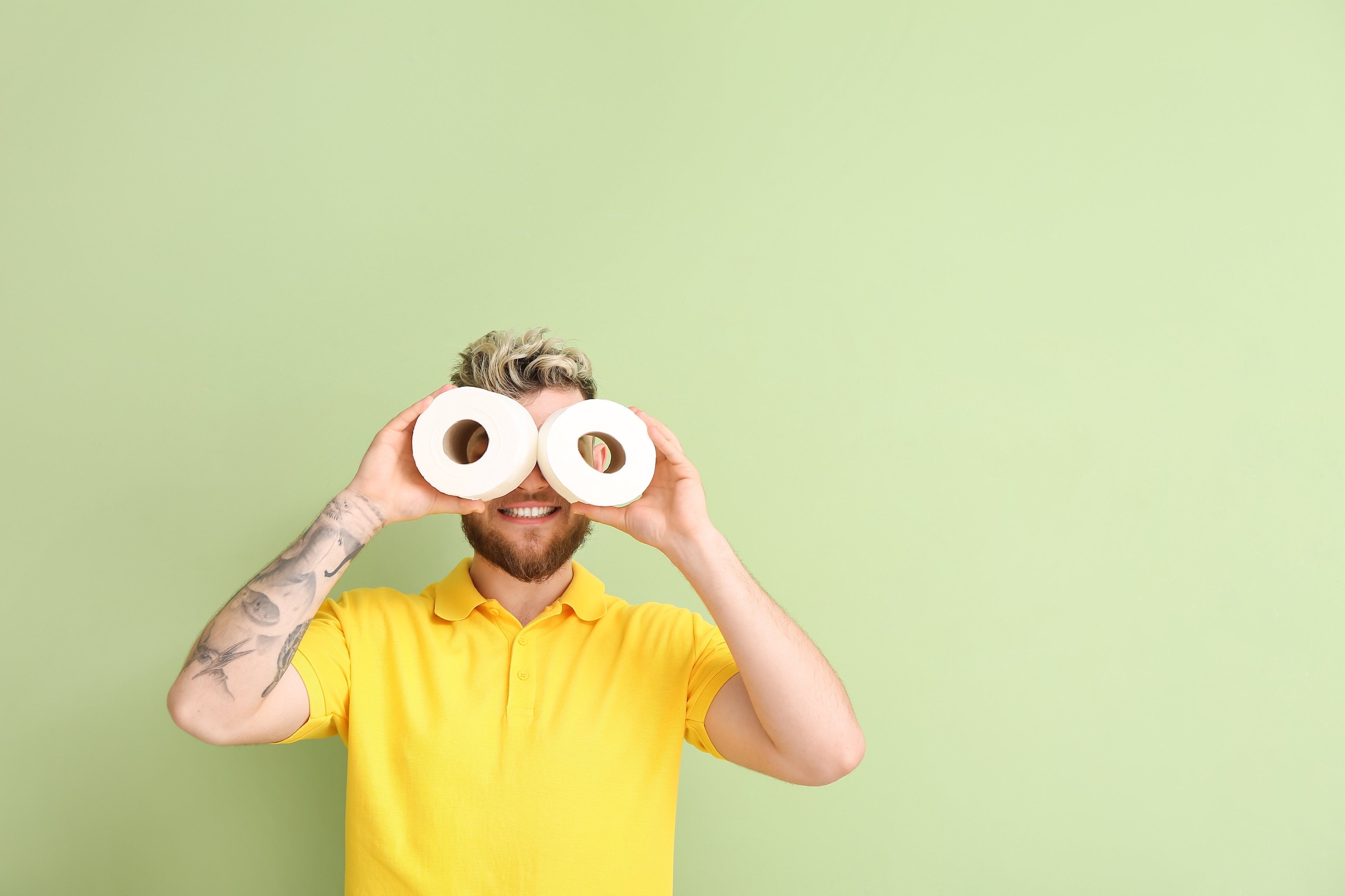 Ein junger Mann mit den Markenfarben von PopoClean, der lachend zwei Klopapierrollen als Augen hält